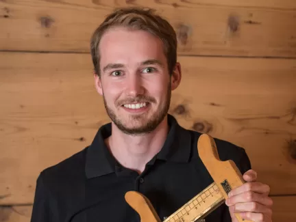 Jan Bucher mit einem alten Werkzeug in der Hand und ein schwarzer Schreinerei Eichenberger Polo Shirt